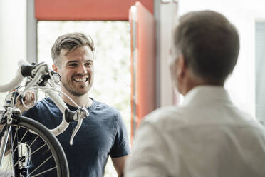 Smiling man carrying bicycle on shoulder while looking at father - GUSF05660