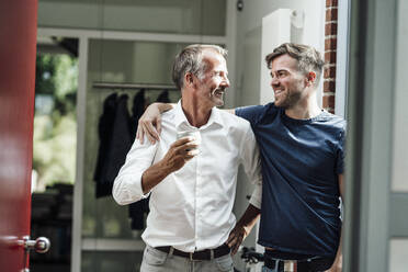 Happy son with arm around father holding coffee cup at home - GUSF05662