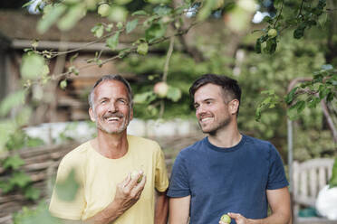 Vater und Sohn halten einen Granny-Smith-Apfel, während sie im Hinterhof stehen - GUSF05677