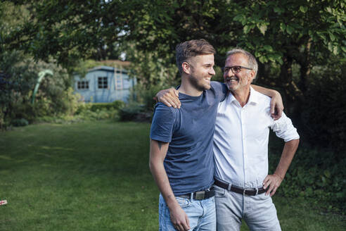 Father and son with arms around standing in backyard - GUSF05705