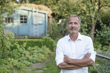 Ernster Mann mit verschränkten Armen im Garten stehend - GUSF05708