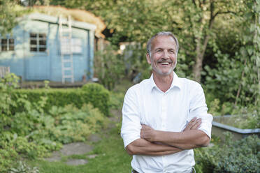 Lächelnder Mann, der mit verschränkten Armen wegschaut, während er im Garten steht - GUSF05709