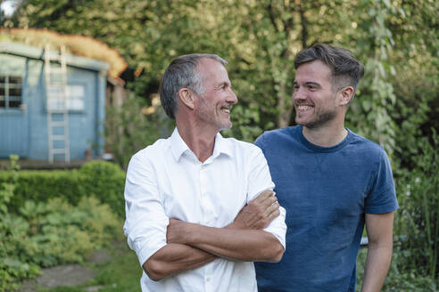 Father with arms crossed looking at son while standing in garden - GUSF05711