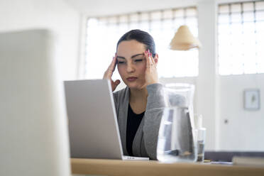 Stressed businesswoman touching head while working at home - GIOF12045