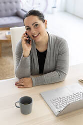 Smiling businesswoman using mobile phone while working at home - GIOF12047