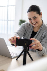 Glückliche Unternehmerin, die während eines Videogesprächs ihr Mobiltelefon auf einem Stativ einstellt - GIOF12050