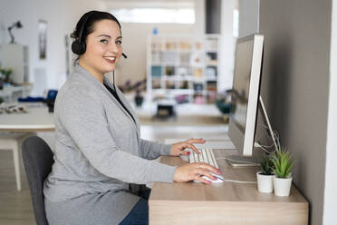 Lächelnde weibliche Kundendienstmitarbeiterin bei der Arbeit am Computer im Heimbüro - GIOF12058