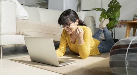 Mature woman using laptop while lying on floor at home - JCCMF01630