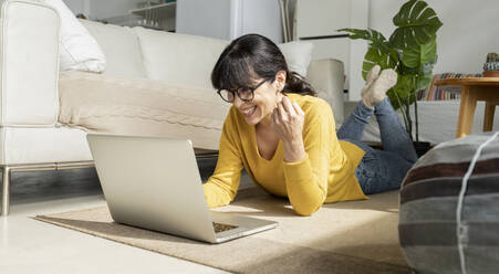 Reife Frau benutzt Laptop, während sie zu Hause auf dem Boden liegt - JCCMF01630