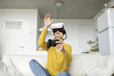 Reife Frau gestikuliert, während sie ein Virtual-Reality-Headset zu Hause trägt - JCCMF01640