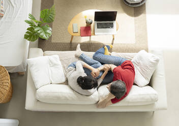 Affectionate couple embracing while sitting on sofa in living room - JCCMF01653