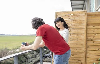 Man leaning on railing while talking to woman in balcony - JCCMF01672