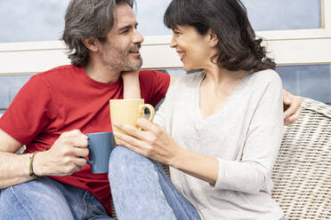 Affectionate couple having coffee while sitting in balcony - JCCMF01675