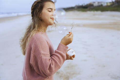 Porträt eines Teenagers, der am Strand Seifenblasen bläst - AZF00217