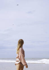 Teenager-Mädchen schaut auf Hubschrauber, die über den Küstenstrand fliegen - AZF00220