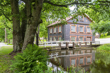 Finnland, Raseborg, Brücke über einen Fluss, der durch einen öffentlichen Park fließt, mit einem traditionellen Haus im Hintergrund - RUNF04221