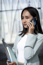 Businesswoman holding diary and laptop while talking on phone - VEGF04169