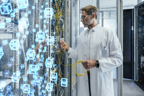 Mature male technician plugging fiber optic cable at data center - LIFIF00011