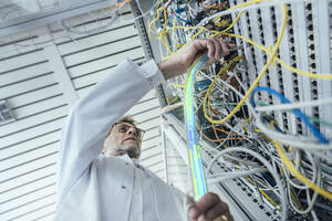 Älterer männlicher IT-Support beim Einstecken von Glasfaserkabeln im Rechenzentrum - LIFIF00013