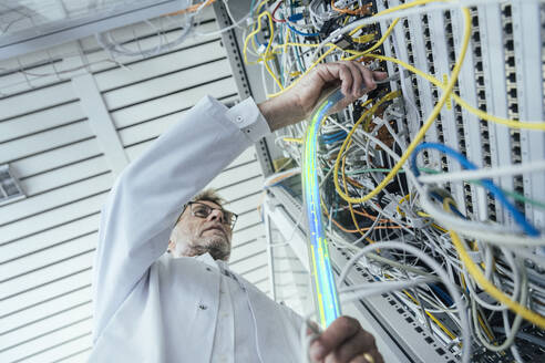 Mature male IT support plugging in fiber optic cable at data center - LIFIF00013