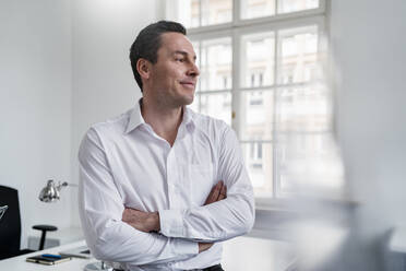 Businessman with arms crossed looking away at office - DIGF14959