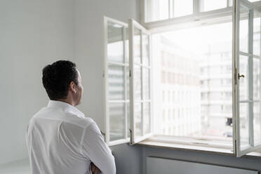 Männlicher Berufstätiger schaut durch ein Fenster im Büro - DIGF14966