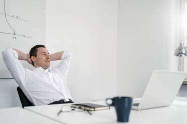 Thoughtful male professional with hands behind head relaxing at office - DIGF14968