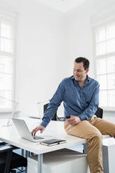 Männlicher Berufstätiger, der am Schreibtisch sitzt und einen Laptop am Arbeitsplatz benutzt - DIGF14974