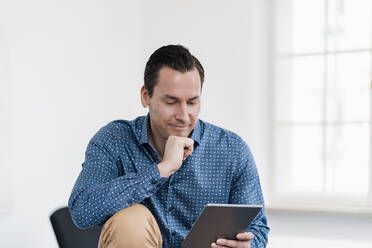 Businessman with hand on chin using digital tablet at workplace - DIGF14975