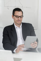 Männlicher Unternehmer, der am Arbeitsplatz sitzt und ein digitales Tablet benutzt - DIGF14995