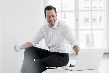 Male professional using laptop while sitting on desk at workplace - DIGF14999