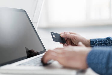 Hand eines männlichen Unternehmers, der einen Laptop benutzt und eine Kreditkarte im Büro hält - DIGF15007