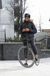 Mann mit Helm benutzt Mobiltelefon auf dem Fahrrad - FBAF01758