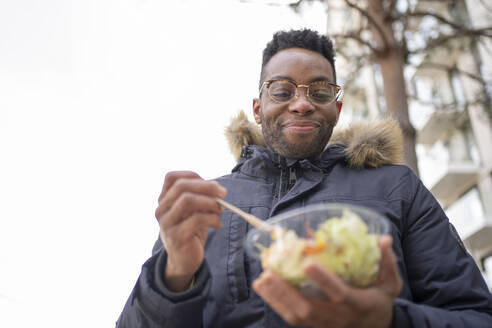 Lächelnder Mann mit Brille beim Salatessen im Winter - FBAF01765