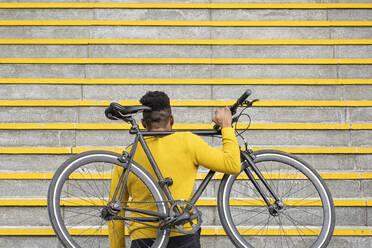 Mann trägt Fahrrad auf der Schulter auf einer Treppe - FBAF01776