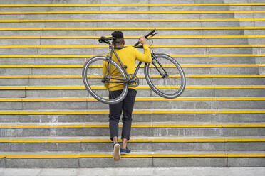 Junger Mann mit Fahrrad auf einer Treppe stehend - FBAF01778