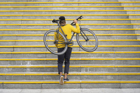 Young man carrying bicycle while climbing on staircase - FBAF01778