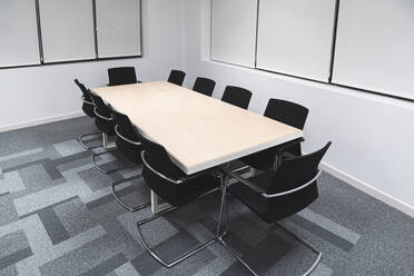 Schwarze Bürostühle um den Konferenztisch im Sitzungssaal am Arbeitsplatz angeordnet - JAQF00445