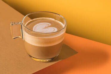 Glastasse mit frischem, heißem, aromatischem Cappuccino mit Latte Art in Form eines Herzens auf dem Tisch serviert - ADSF22443