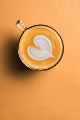 Glastasse mit frischem, heißem, aromatischem Cappuccino mit Latte Art in Form eines Herzens auf dem Tisch serviert - ADSF22444