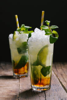 Gläser mit kaltem Alkohol Mojito-Cocktail mit Rum und frischen Limetten, serviert mit Eis und Minzblättern auf einem Holztisch - ADSF22449
