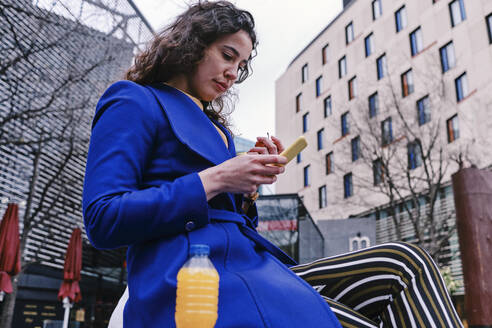 Geschäftsfrau, die ein Smartphone benutzt, während sie an einer Saftflasche sitzt - ASGF00120