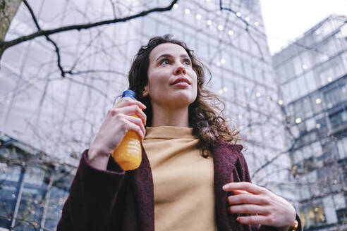 Nachdenkliche Frau, die eine Flasche Saft hält und wegschaut - ASGF00123