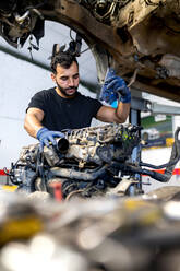 Serious male mechanic with flashlight examining lifted car while working in automobile service - ADSF22475