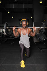 Muskulöser Mann, der eine Langhantel hebt, während er im Fitnessstudio eine Ausfallübung macht - AODF00450
