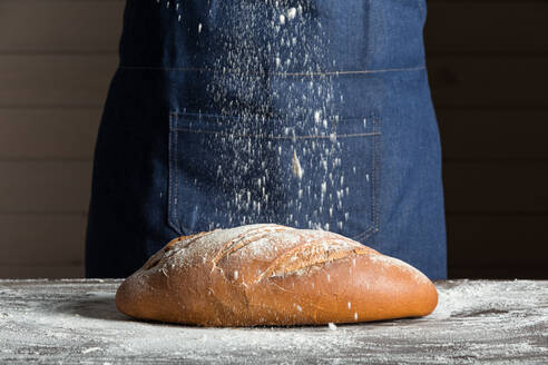 Anonymer Bäcker beim Bestreuen eines frischen Brotlaibs auf dem Tisch in einer Bäckerei - ADSF22488