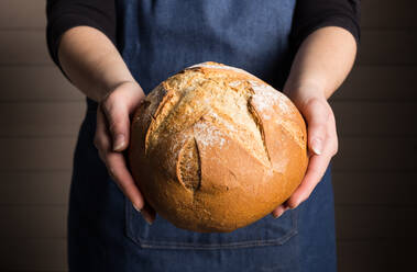 Anonymer Bäcker in Schürze demonstriert frisch gebackenes, aromatisches, knuspriges Brot - ADSF22489