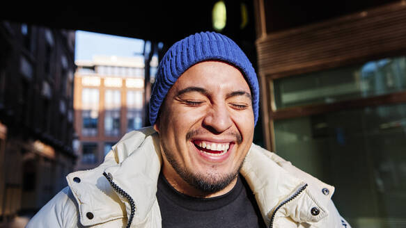 Young man wearing knit hat laughing during sunny day - ASGF00132