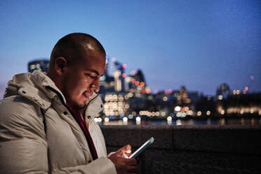 Junger Mann benutzt Smartphone in der Stadt bei Nacht - ASGF00146