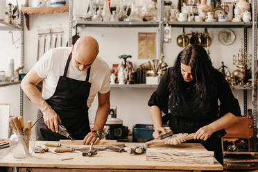 Konzentrierter reifer Handwerker und Frau mit professionellen Werkzeugen bei der Herstellung von Holzdetails in der Kunstwerkstatt - ADSF22494
